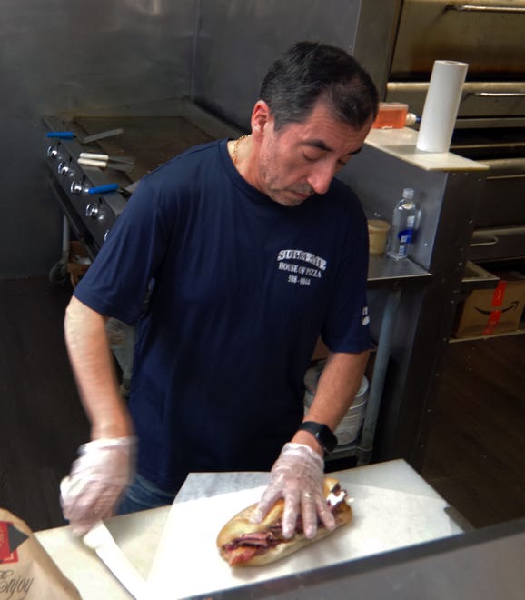 Carlos Catalan of the Supreme House of Pizza puts the finishing touches on a sandwich for a customer during a busy period on Tuesday, Nov. 14, 2023.