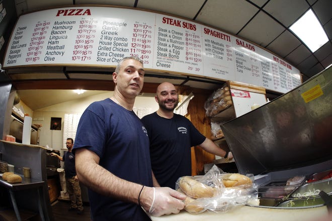 Tim Follo and owner Manny Lambrakis stand in front of the menu at the Supreme House of Pizza in Brockton on Tuesday, Nov. 14, 2023. While famous for their steak & cheese sandwich, the restaurant also makes a variety of meals, from pizza, to hot and cold sandwiches, to full dinners.